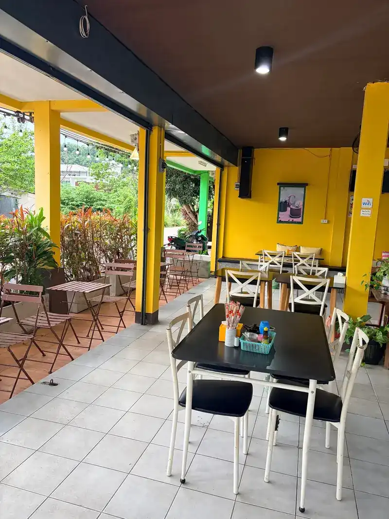 The covered terrace: black tables, white chairs and yellow pillars, with plants along the edge