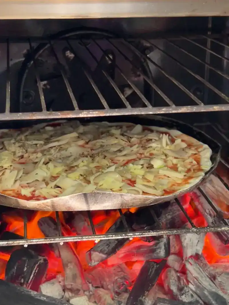 A pizza baking on a rack above glowing charcoal