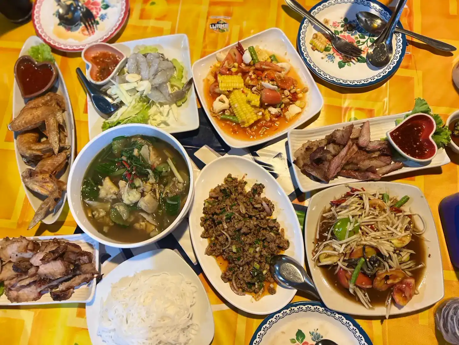 A full table of Isaan dishes shared on a yellow tablecloth, seen from above