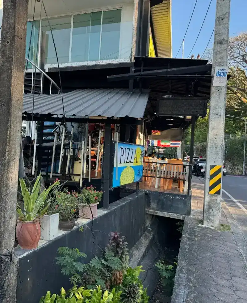 The restaurant from the street: a terrace with orange chairs and a blue PIZZA sign