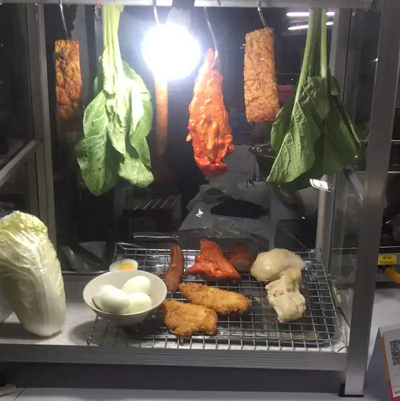 The lit glass cabinet after dark, with red pork, greens and eggs