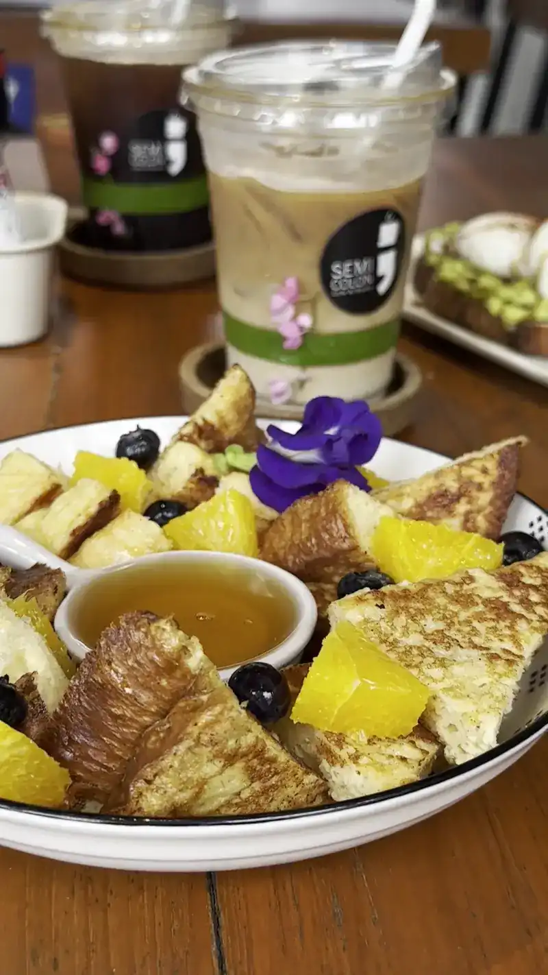 Golden toast, a croissant, pineapple and blueberries with a small pot of syrup, an iced coffee behind