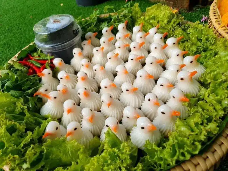 Rows of white bird-shaped dumplings with orange beaks on lettuce