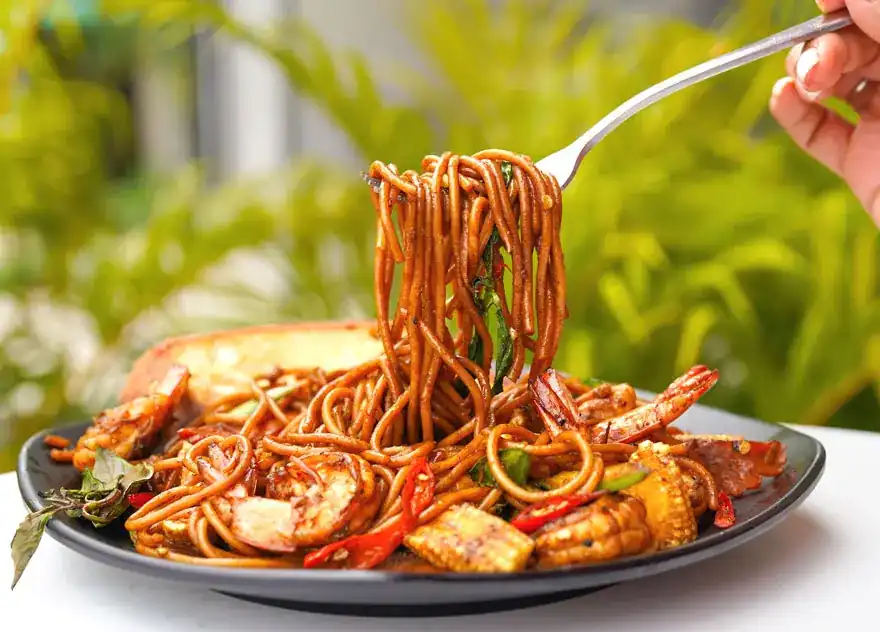 A fork lifting stir-fried noodles with prawns, chilli and basil from a dark plate
