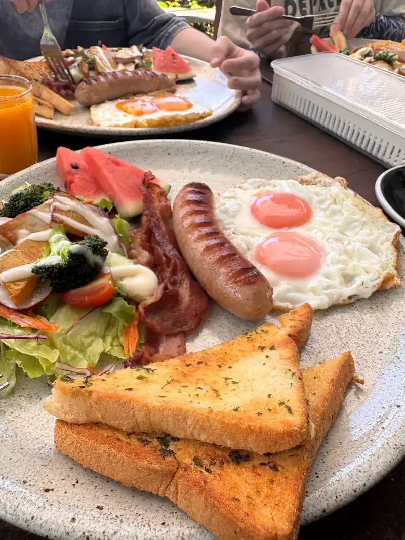 Breakfast plate with two fried eggs, sausage, bacon, salad, watermelon and garlic toast