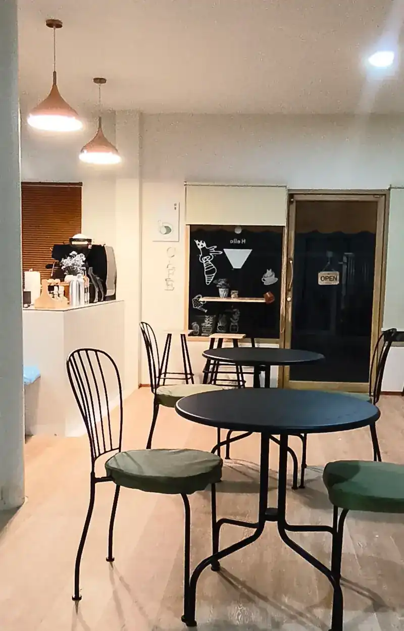 Inside FA&NA: round black tables, green seat cushions, pendant lamps and the coffee counter