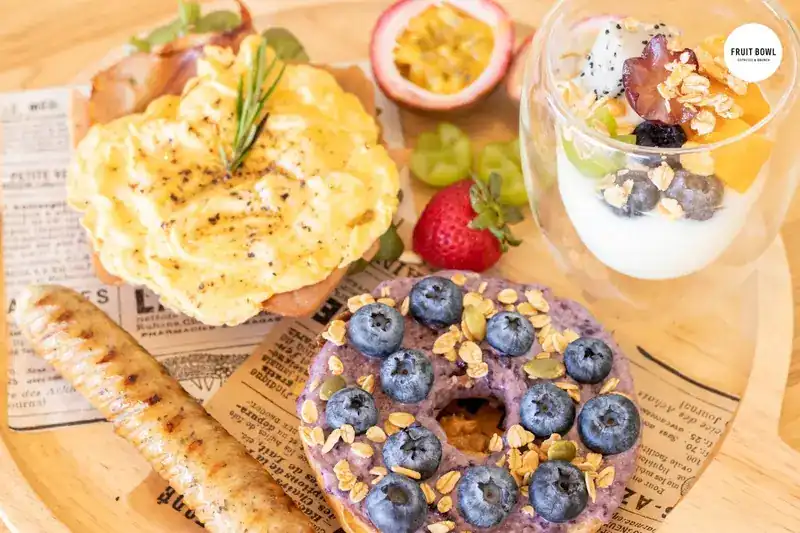 Scrambled egg, a grilled sausage, a blueberry bagel with granola and a cup of yogurt with fruit