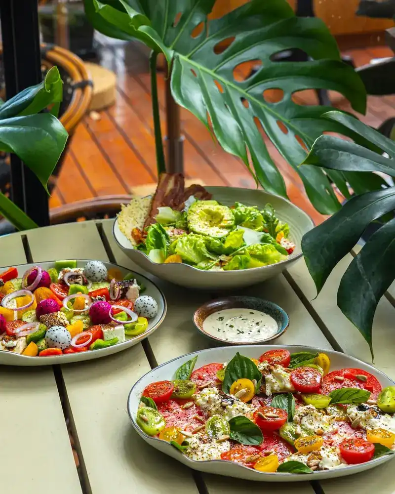 Three salads on a garden table under monstera leaves