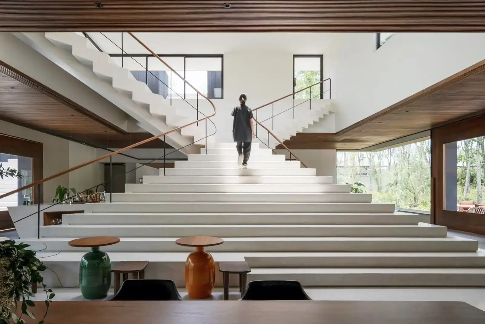 The wide white staircase inside Tree O’clock, with timber handrails and a figure walking up, seen from behind