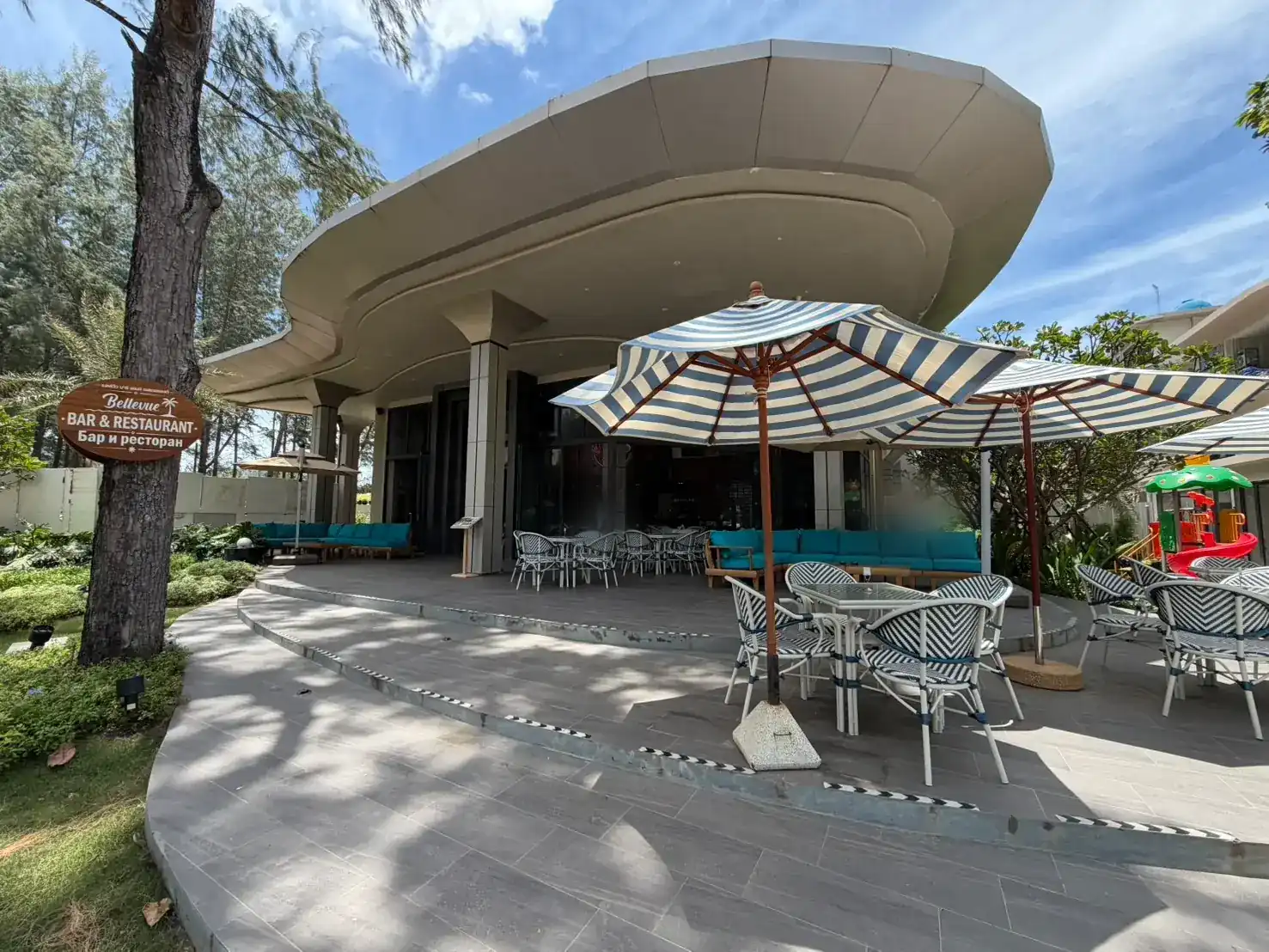 Bellevue's terrace under its white curved canopy roof, with navy-striped umbrellas and blue-and-white bistro chairs
