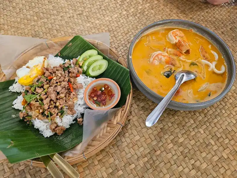 Minced pork stir-fry on rice with a fried egg, next to a creamy tom yum with prawns and squid