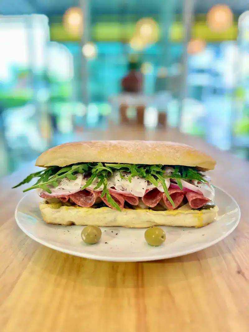 Salami sandwich with rocket on a long roll, olives on the side