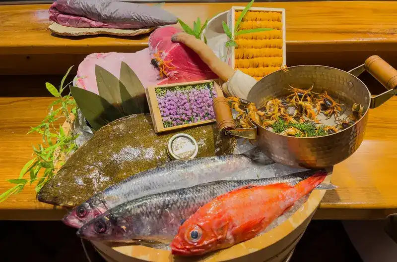 Whole fish on ice in a wooden tub, with a tray of sea urchin and a block of tuna on the counter