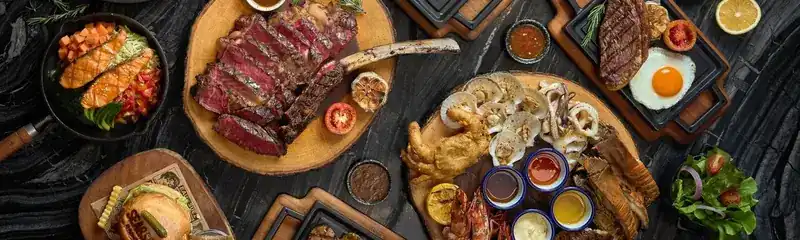 A table seen from above with a sliced tomahawk steak, a seafood platter, salads and sauces