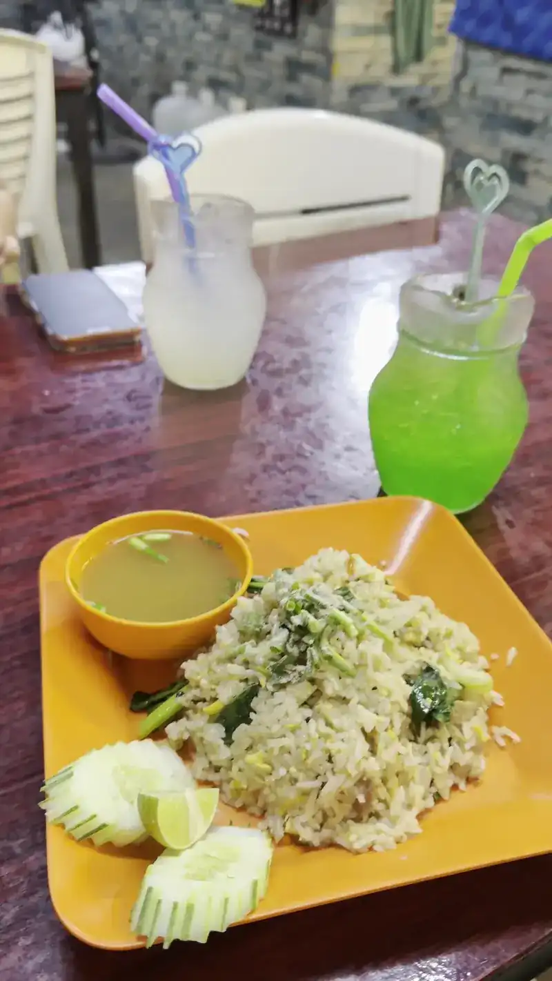 Fried rice with a cup of soup on an orange plate, two iced drinks behind it on a dark wooden table