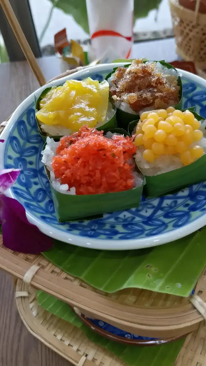 Sticky rice in banana-leaf cups with four different toppings on a blue and white plate