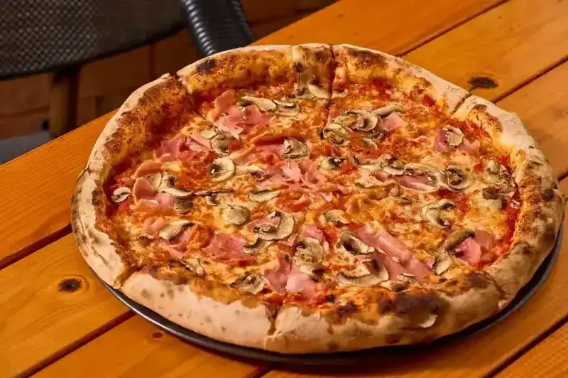 Pizza with ham and mushrooms, its crust blistered from the oven