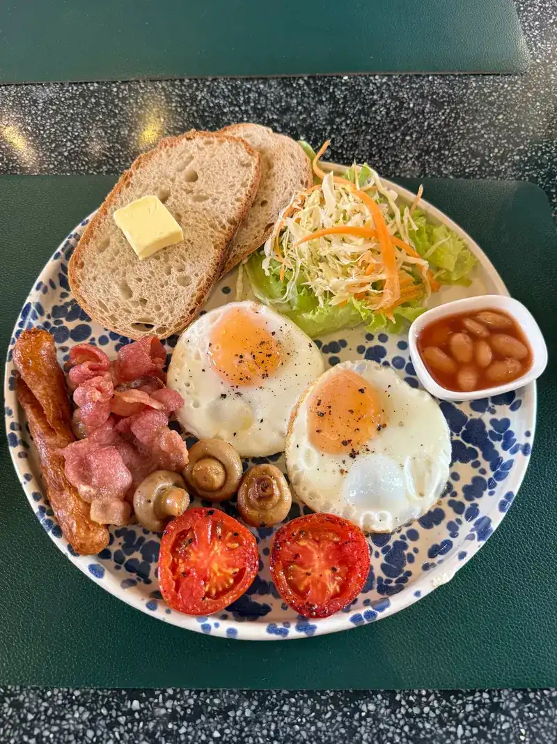 An English breakfast from above: fried eggs, bacon, sausage, mushrooms, tomatoes, beans and toast