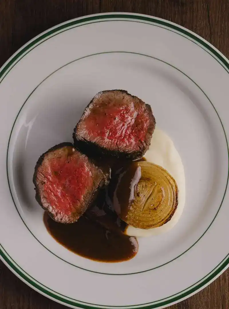 Two cuts of tenderloin with a roasted onion on a green-rimmed plate