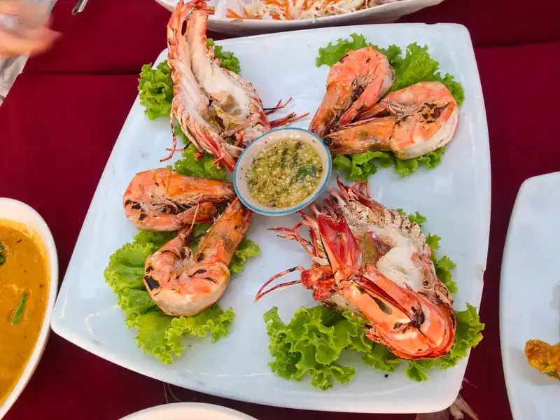Grilled prawns around a small bowl of green seafood sauce