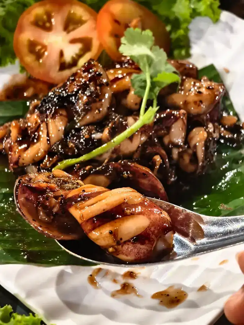 Pieces of squid with a dark, glossy glaze on a banana leaf