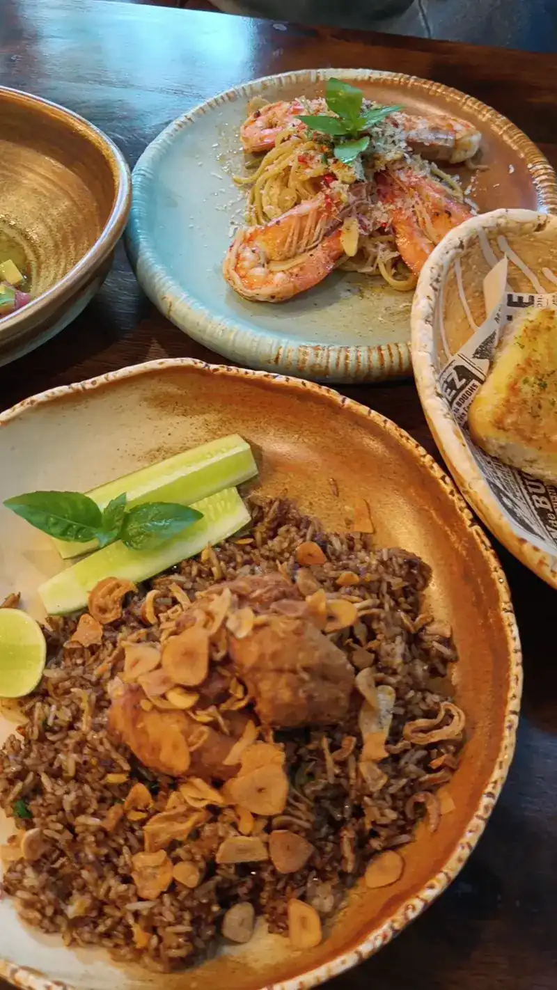 Rice under crispy garlic with cucumber, prawn pasta and garlic bread on a wooden table