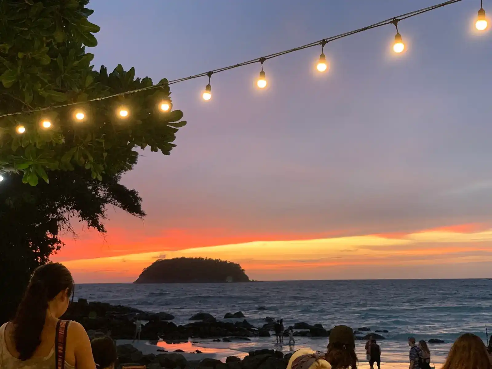 Sunset over the little island in the bay, seen from under the string lights at Kata Bar.B.Q