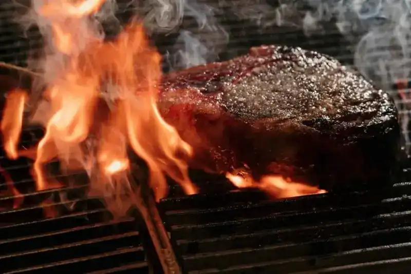 A thick steak on the grill bars with flames rising beside it