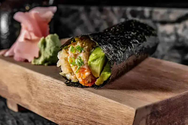 A crab and avocado hand roll with shrimp roe on a wooden stand
