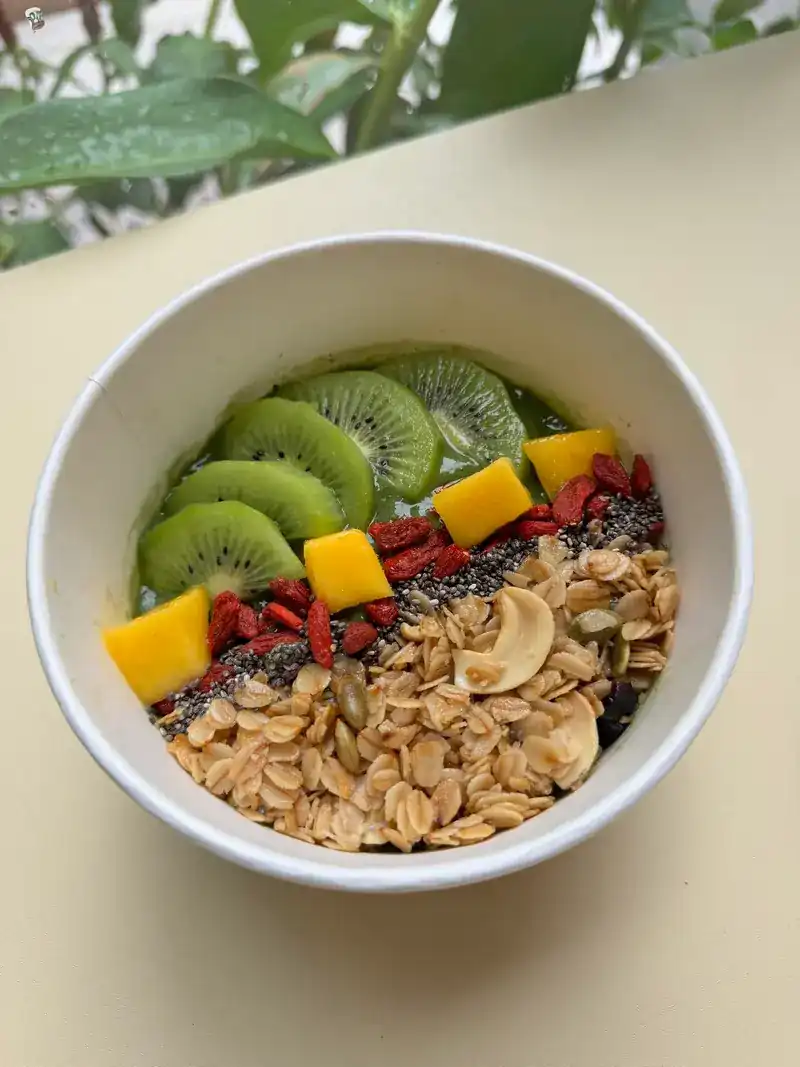 Green smoothie bowl topped with kiwi, mango, goji berries, seeds and granola