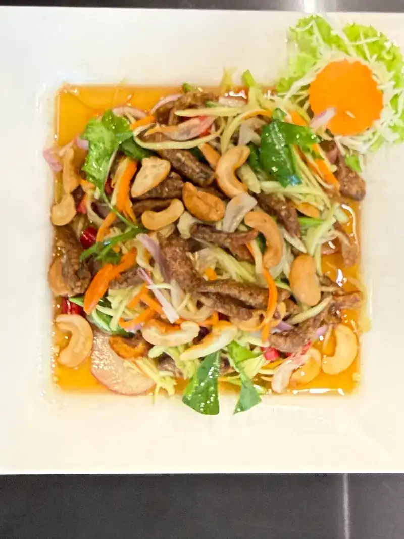 A salad of cashew nuts, crisp meat strips, carrot and greens on a white plate