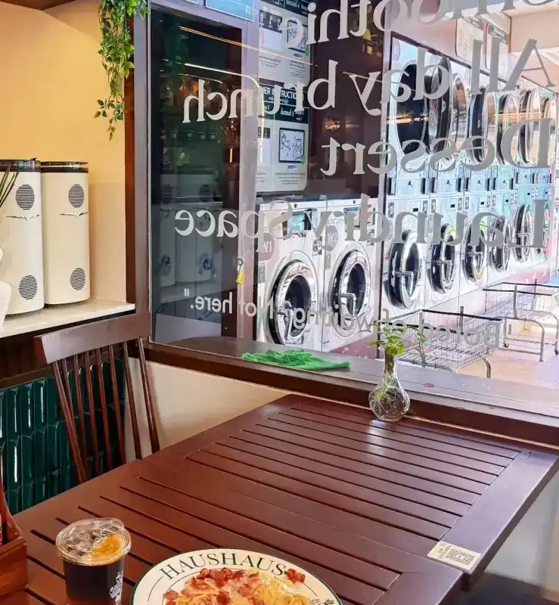 A café table by the glass wall, with washing machines and the window lettering behind it
