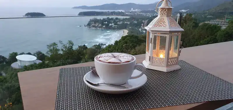 A cappuccino and a white lantern on a table at the rail, the bays and the sea below / คาปูชิโน่กับโคมไฟสีขาวบนโต๊ะริมราว มองเห็นอ่าวและทะเลเบื้องล่าง