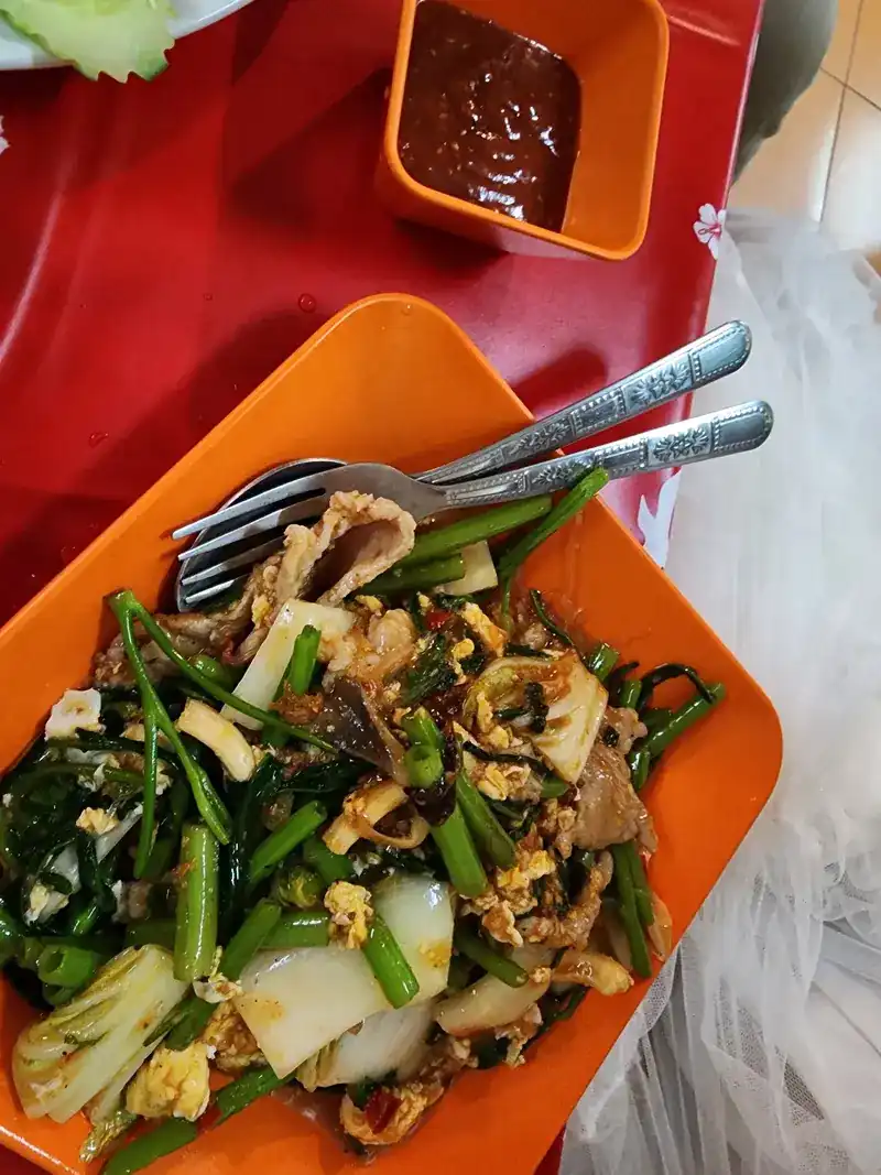 Stir-fried morning glory, cabbage, egg and meat on an orange plate