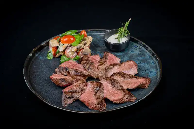 Sliced grilled beef with a mushroom and tomato salad and a white sauce on a blue plate