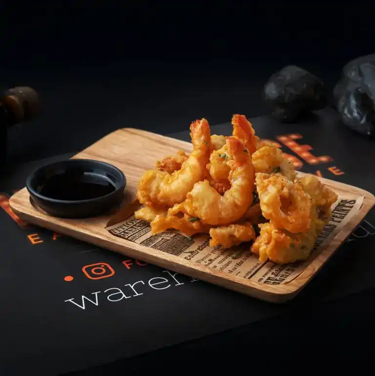 Tempura prawns on a wooden board with a dipping sauce