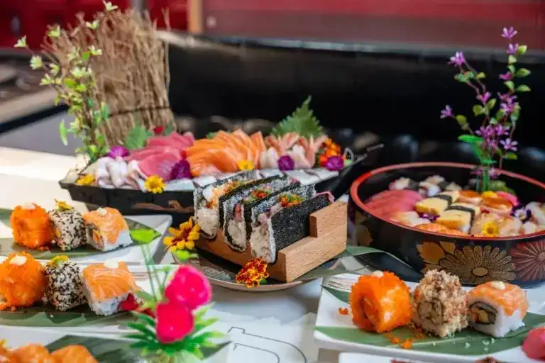 A table of sushi rolls, salmon sashimi and a chirashi bowl dressed with flowers