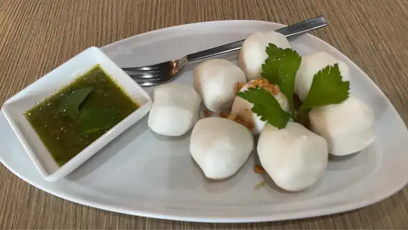 Fish balls on a white plate with a green dipping sauce and coriander