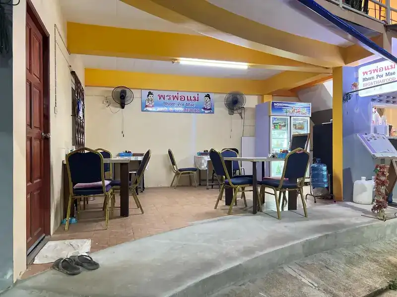 The open-fronted dining room with blue chairs, yellow beams and the Bhorn Por Mae sign on the wall