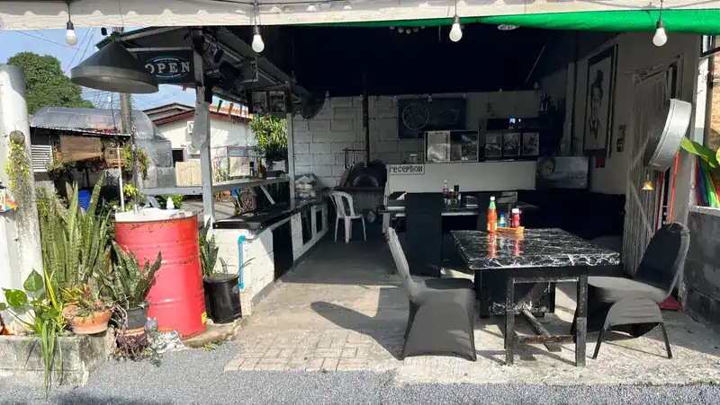 The shop front by day: an open terrace with a red oil drum, plants and a marble table