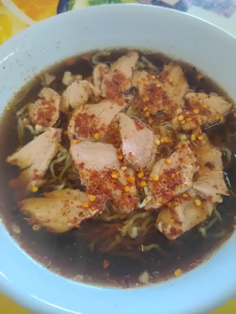 Sliced duck over yellow egg noodles in a dark broth, with chilli flakes on top