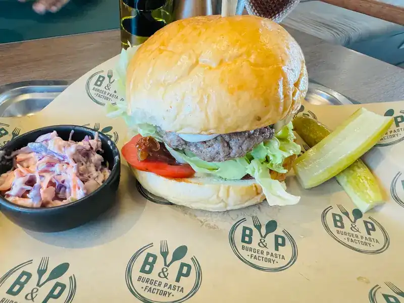 A beef burger with coleslaw and a pickle on B&P tray paper