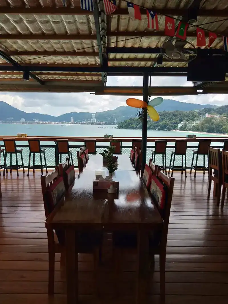 The terrace with long wooden tables, open to the bay and the Patong hills