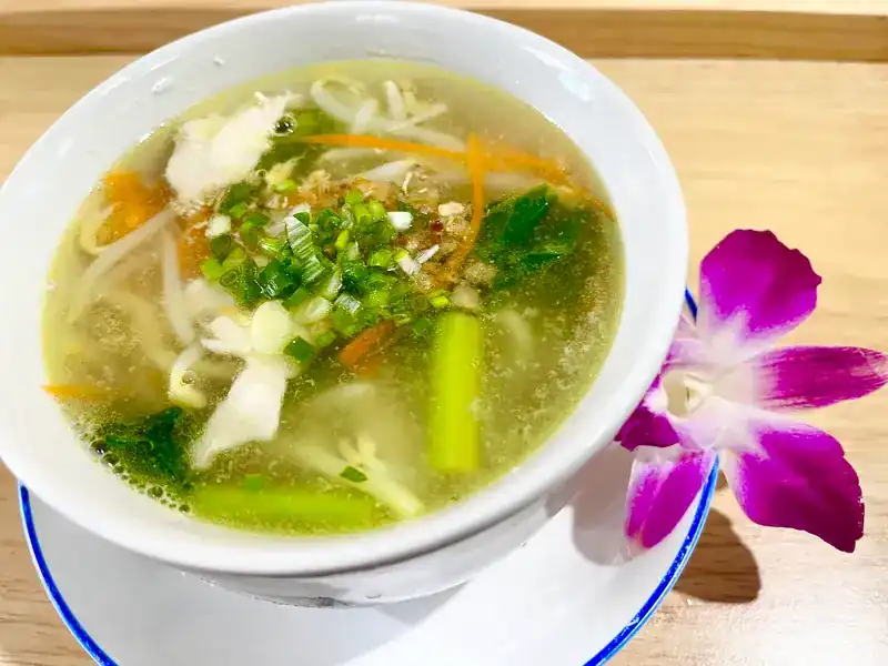 Clear noodle soup with bean sprouts and spring onion, an orchid beside the bowl