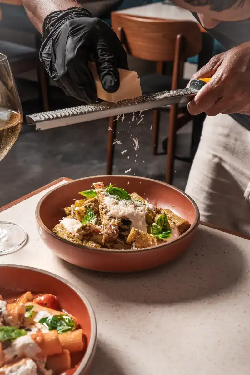 Cheese being grated over a bowl of rigatoni at the table