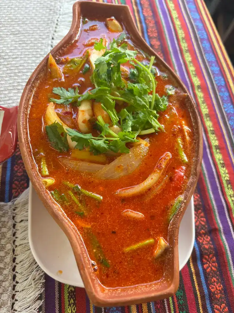 A red, spicy-looking seafood soup with coriander in a fish-shaped clay bowl