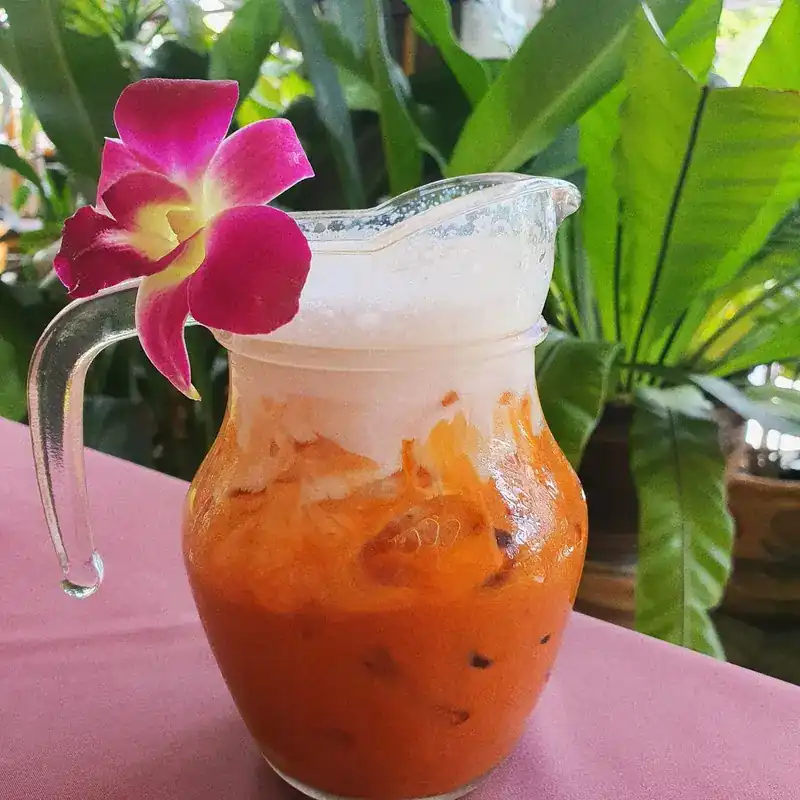 Thai iced tea in a glass jug with a purple orchid, on a pink tablecloth