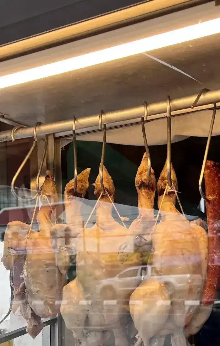 Whole chickens hanging on hooks under the light of the glass case