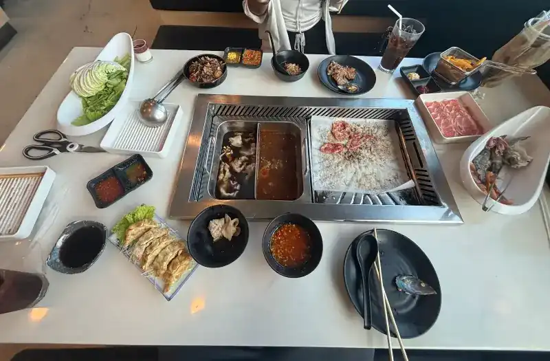A table mid-meal with the two-part pot, the grill plate, gyoza and dipping sauces