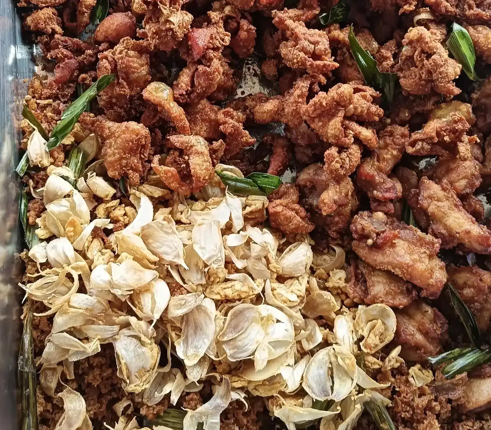 A steel tray of bite-size fried chicken with crisp garlic cloves and green herb leaves